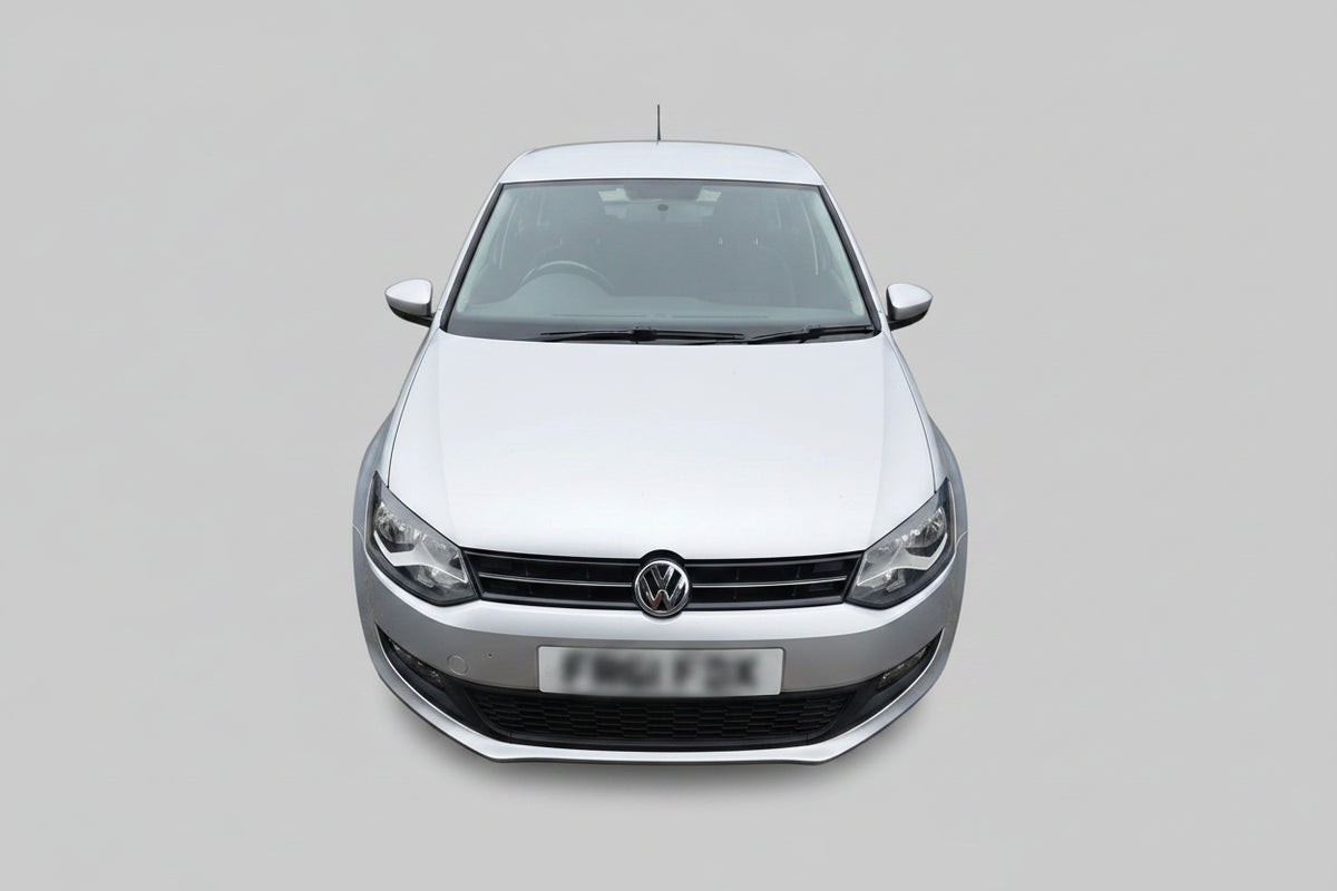 A silver Volkswagen Polo hatchback parked outdoors on a dirt lot, showing the front grille, headlights, and front license plate.